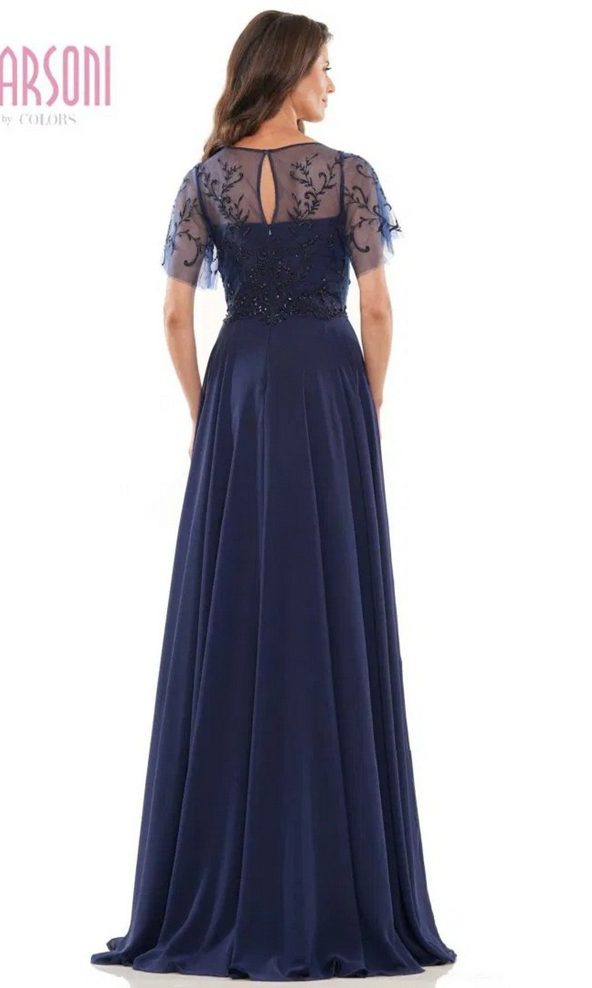 A woman is wearing the Marsoni M323 long formal dress, a navy blue chiffon gown featuring sheer short sleeves, a floral beaded embroidered bodice, and a keyhole back.